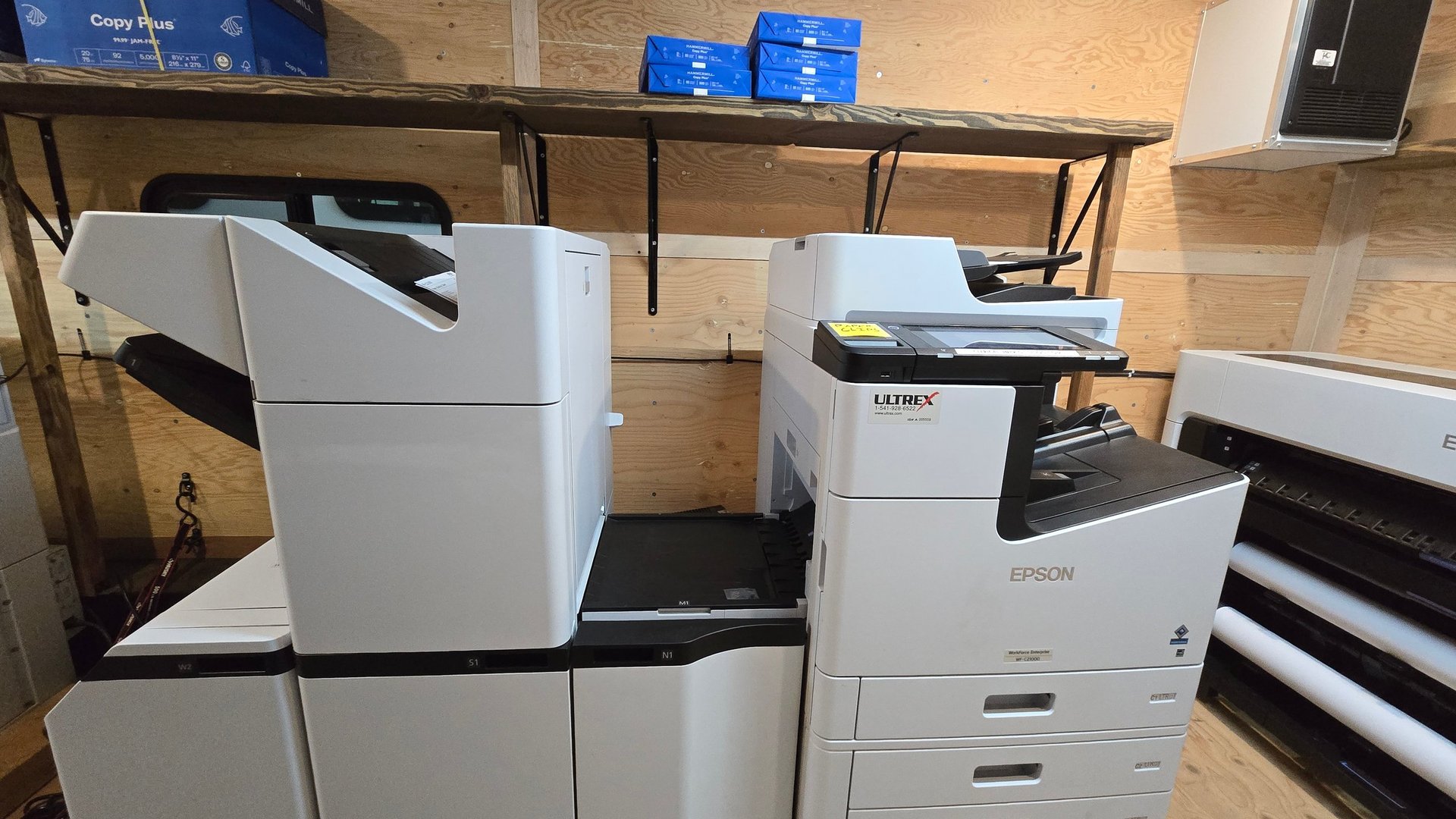 Office equipment including white printers and copiers arranged on shelving in a storage room