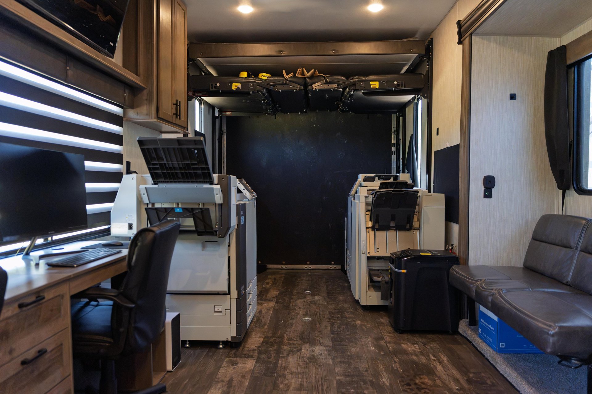 Interior of an RV with cockpit, kitchen appliances, dining area, and lounge seating along wooden floors