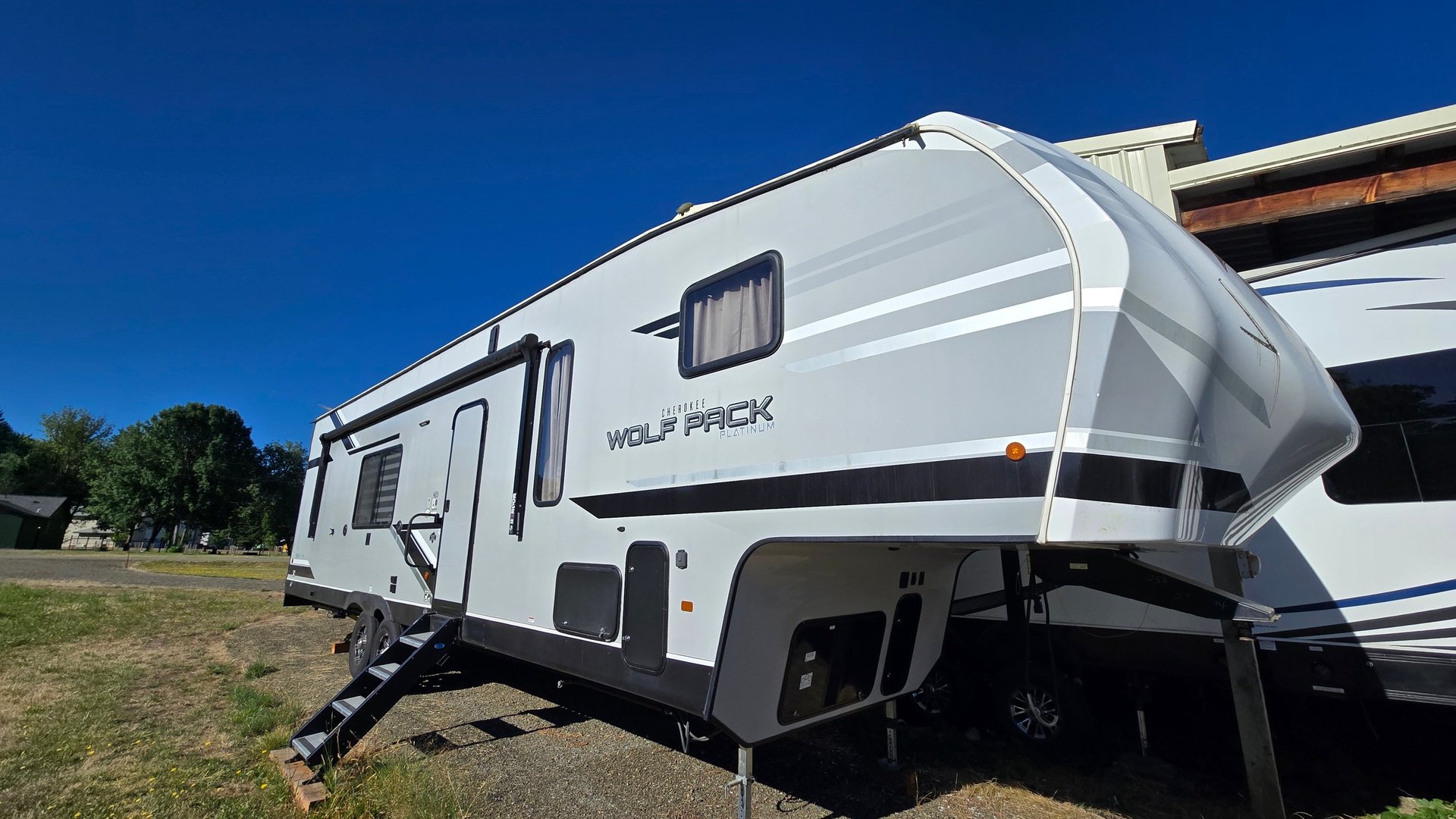 White Wolf Pack travel trailer RV parked in grass lot under clear blue sky, side angle view showing exterior design